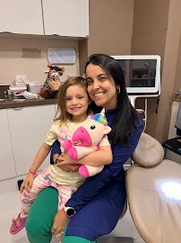 Dra. Esther Martins sentada com uma criança no colo, no consultório odontológico.